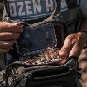 A man prepares his fishing tackle by a river, organizing equipment for outdoor fishing.
