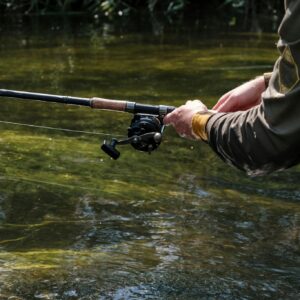 A person enjoying fishing on a calm river with a rod and reel, showcasing leisure activity.